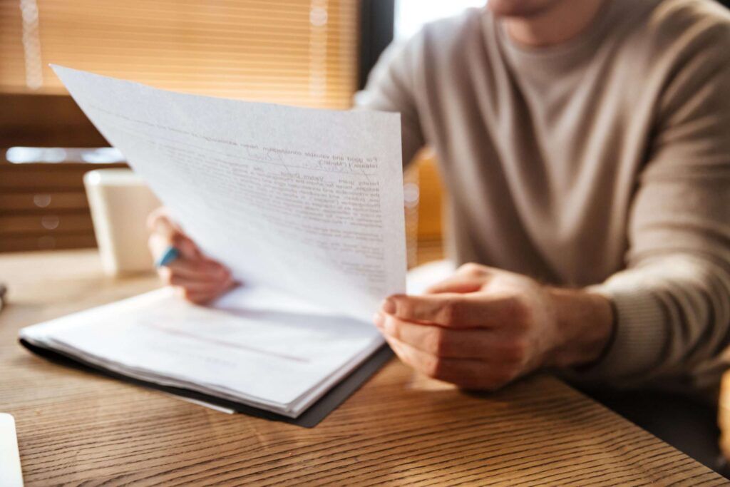Person prüft ein mehrseitiges Gutachten in einer Dokumentenmappe am Schreibtisch